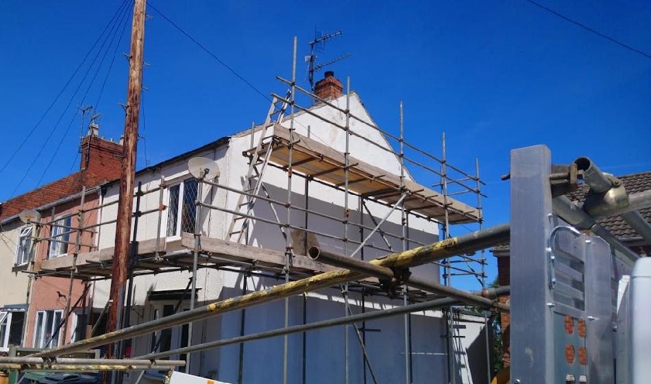 Gable end scaffold on a rendered terrace against a clear sky